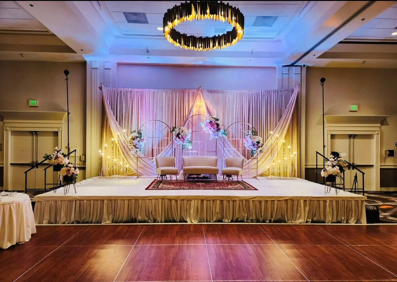A wide blush and ivory event stage framed by candlelight and draped fabric