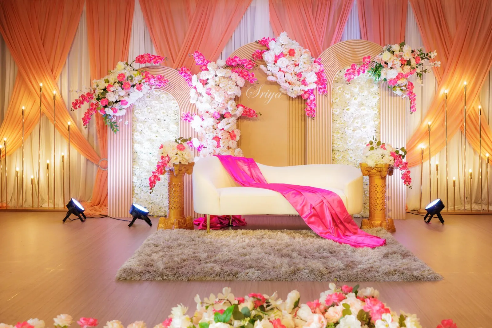 A peach, pink and ivory floral event stage with curved panels and a white lounge