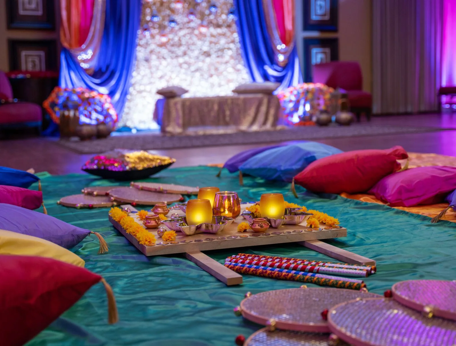 A colorful mehndi floor setting with teal fabric, bright cushions and candlelight